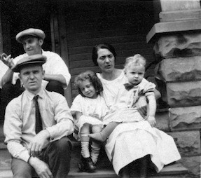 Family group on porch: two men in caps, woman, two children