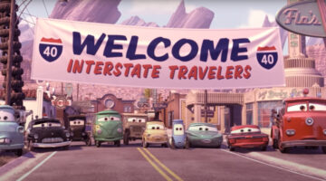 A still from the Disney animate movie Cars should a line-up of Cars characters (all automobiles of varying makes and models, including a firetruck). They are lined up under a large banner straddling “Radiator Springs” main street. The sign reads “WELCOME INTERSTATE TRAVELERS.” But the trouble is that no interstate travelers have arrived. The cars look somewhat anxious and dismayed.