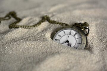 Image of a pocket watch and chain partially buried in sand.