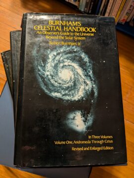 Photograph showing the first volume of Burnham's Celestial Handbook, with the other two volumes stacked below it.